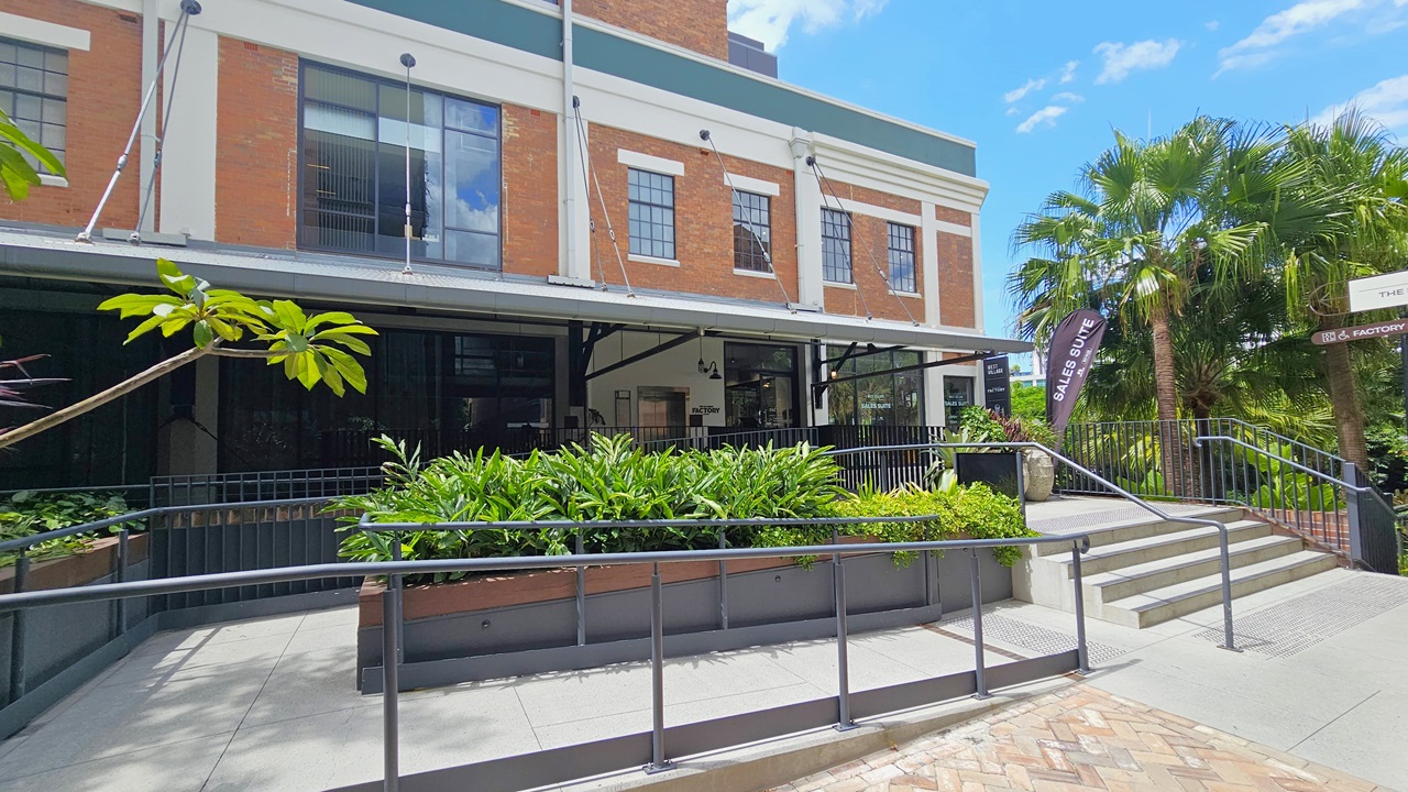 A staircase and ramp with handrails provide access to a two-storey brick building, with truncated domes installed before them. Ornamental plants adorn the concrete planter box in front. Palm trees and additional trees and ornamental plants are situated to the right. Signages are placed on the building's corner. A staircase and ramp with handrails provide access to a two-storey brick building, with truncated domes installed before them. Ornamental plants adorn the concrete planter box in front. Palm trees and additional trees and ornamental plants are situated to the right. Signages are placed on the building's corner.