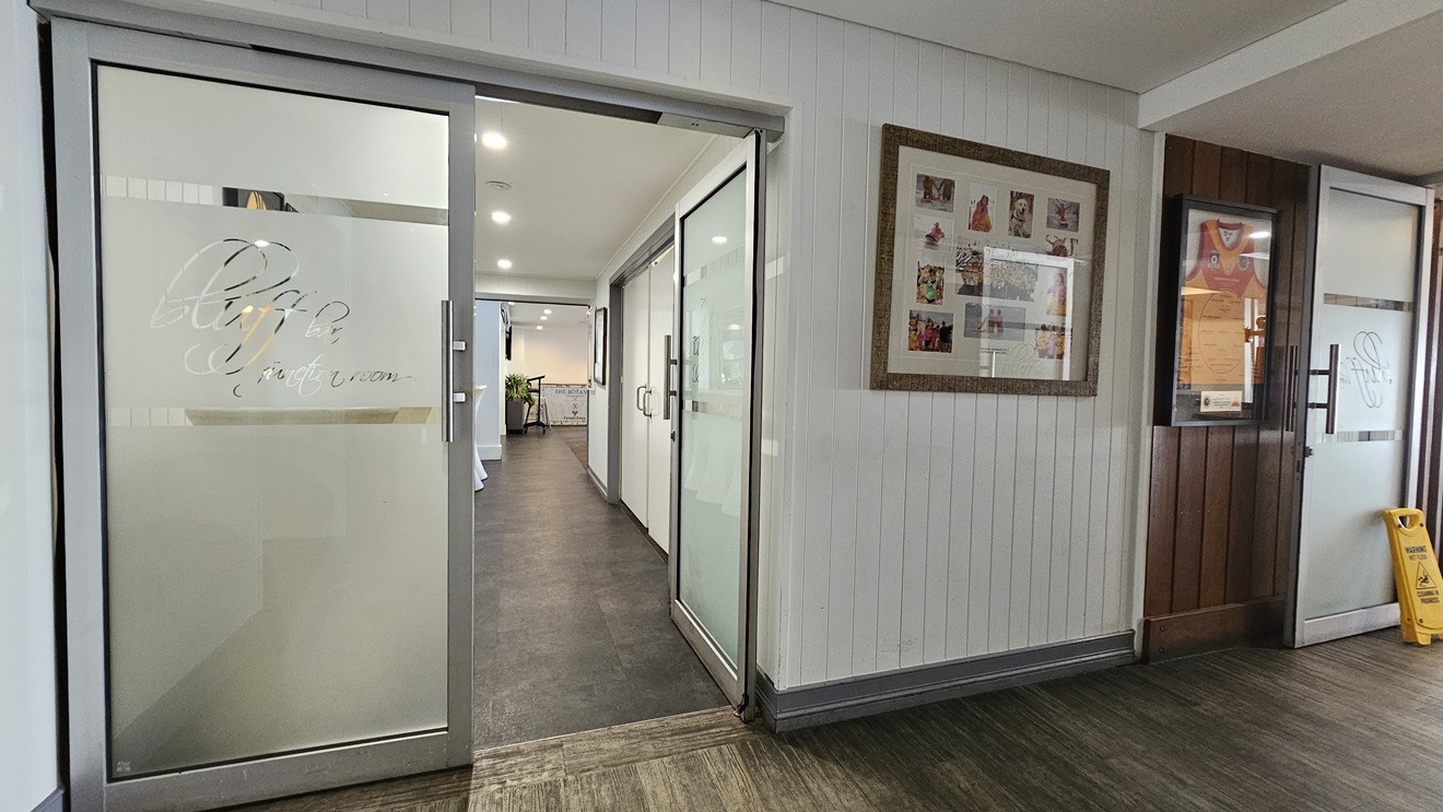 On the left, there is a glass door with "Bluff" etched on it, leading to a hallway with white walls and dark flooring. In the middle, there is another glass door with the same etching, also leading to the hallway.The hallway extends to a well-lit area with white cabinets. On the right, there is a white panelled wall with a large framed collage of photos and a wooden panelled section with a bulletin board. The floor has timber and the ceiling is white with recessed lighting. On the left, there is a glass door with "Bluff" etched on it, leading to a hallway with white walls and dark flooring. In the middle, there is another glass door with the same etching, also leading to the hallway.The hallway extends to a well-lit area with white cabinets. On the right, there is a white panelled wall with a large framed collage of photos and a wooden panelled section with a bulletin board. The floor has timber and the ceiling is white with recessed lighting.