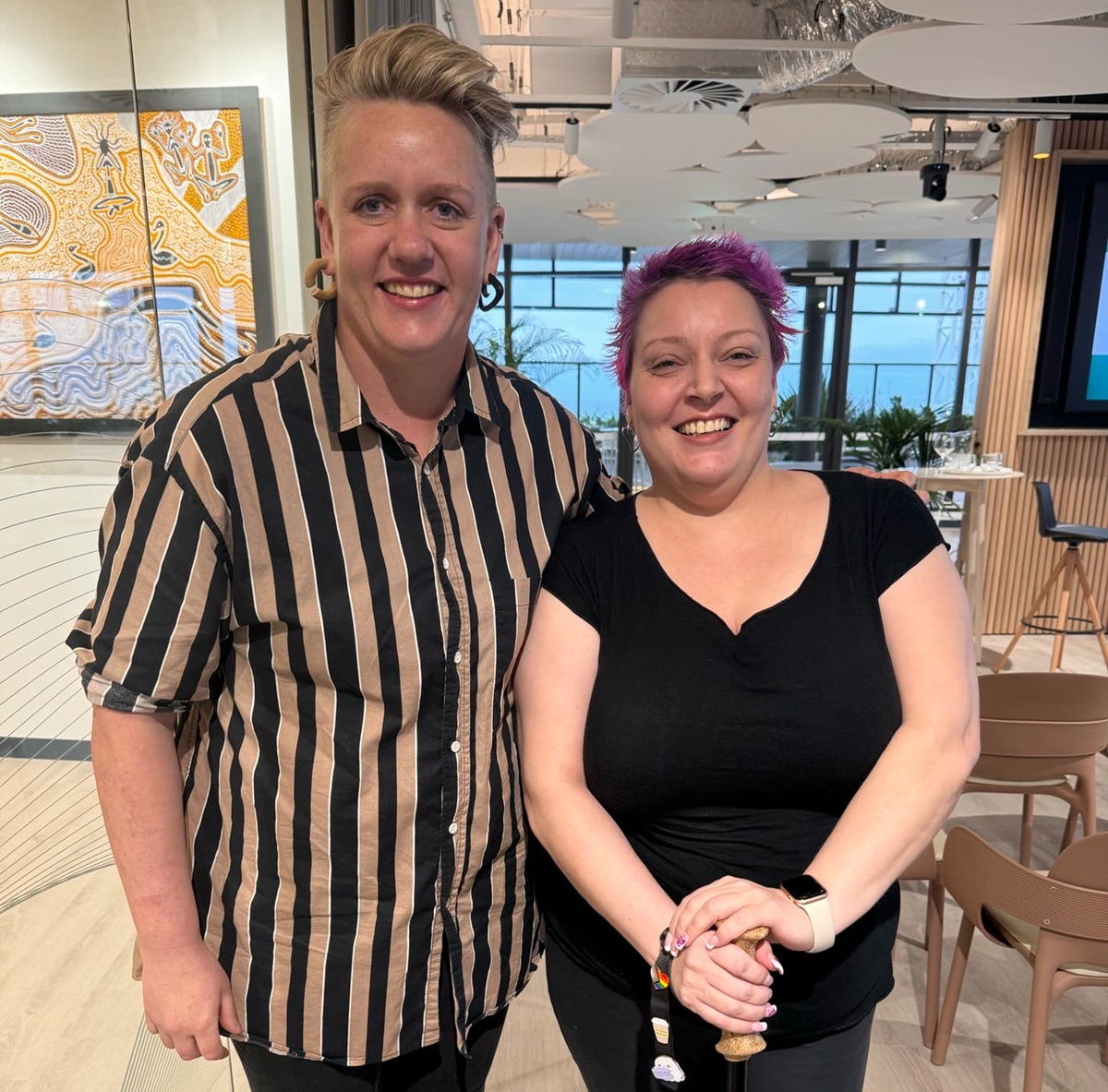 Two people smiling indoors, posing together for a photo. Two people smiling indoors, posing together for a photo.