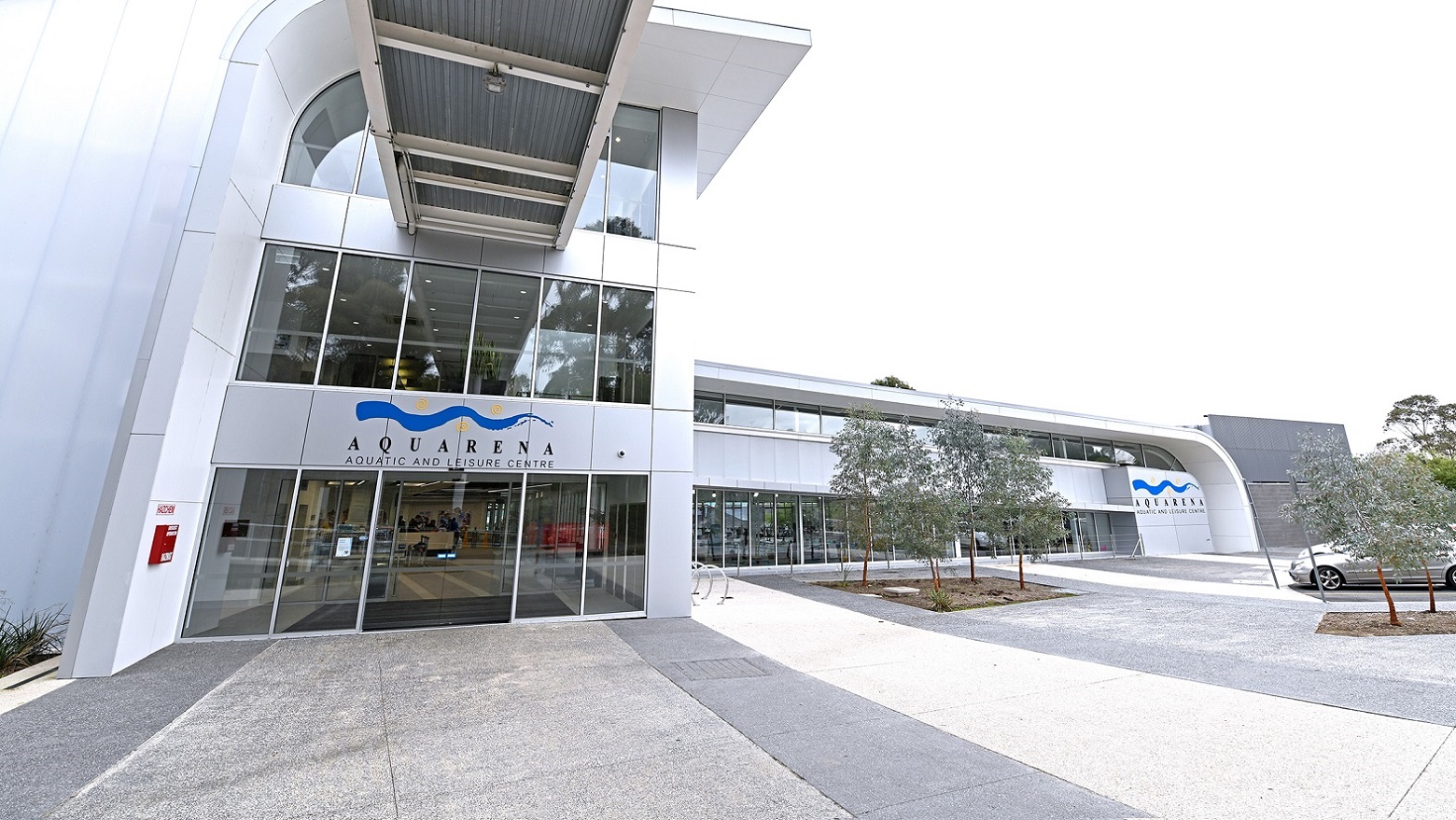 Main entrance of Aquarena Aquatic and Leisure Centre. The Aquatic Center is located within a vast, naturally-formed amphitheater with gently sloping hillsides, occupying more than 11 acres of beautifully landscaped gardens. It boasts a combination of both indoor and outdoor amenities. Furthermore, the building incorporates numerous glass windows, allowing for interior visibility from the outside, and it features a sky bridge spanning above the entrance. Main entrance of Aquarena Aquatic and Leisure Centre. The Aquatic Center is located within a vast, naturally-formed amphitheater with gently sloping hillsides, occupying more than 11 acres of beautifully landscaped gardens. It boasts a combination of both indoor and outdoor amenities. Furthermore, the building incorporates numerous glass windows, allowing for interior visibility from the outside, and it features a sky bridge spanning above the entrance.