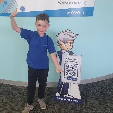 A boy in a blue shirt stands next to a Cérge cartoon cutout with a QR sign. A boy in a blue shirt stands next to a Cérge cartoon cutout with a QR sign.