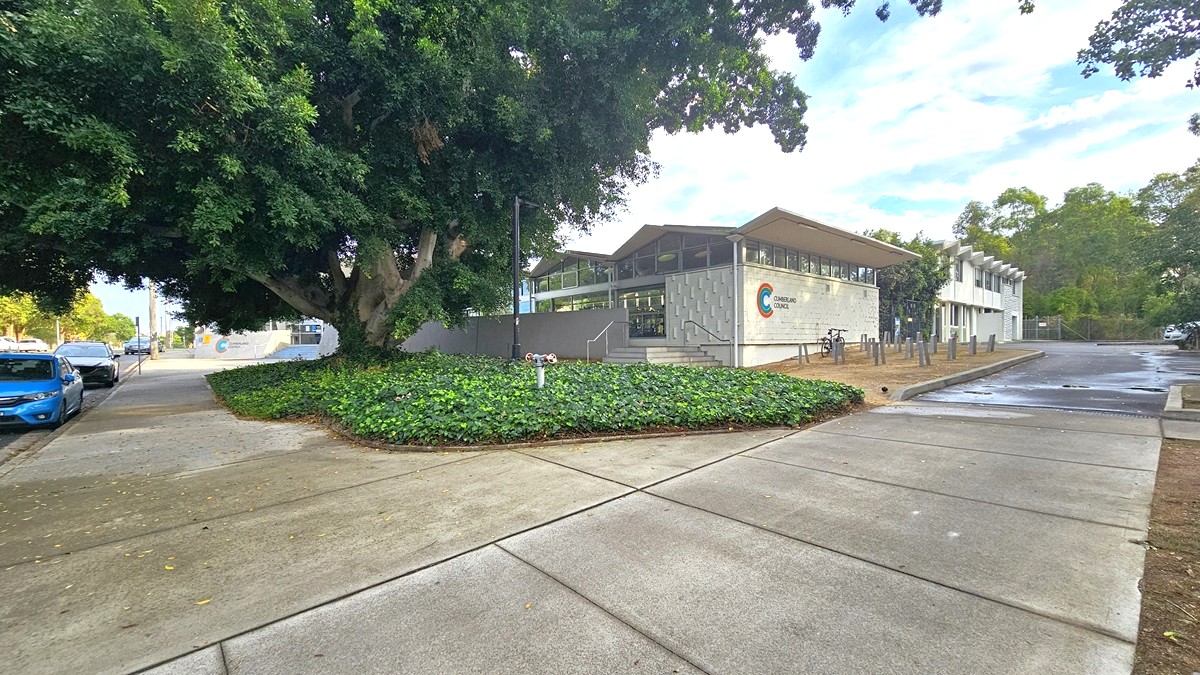 A garden filled with green plants, a large tree at the center, and a black lamp post features the right front area of the facility. There is a short staircase with metal handrails leading to another entry point to the centre. The left white brick wall has narrow rectangular white bricks protruding from the wall while the right brick wall has green, blue, and red color lines forming a C beside ‘CUMBERLAND COUNCIL.’ The space in front is filled with pairs of grey wood in an upright position. A garden filled with green plants, a large tree at the center, and a black lamp post features the right front area of the facility. There is a short staircase with metal handrails leading to another entry point to the centre. The left white brick wall has narrow rectangular white bricks protruding from the wall while the right brick wall has green, blue, and red color lines forming a C beside ‘CUMBERLAND COUNCIL.’ The space in front is filled with pairs of grey wood in an upright position.