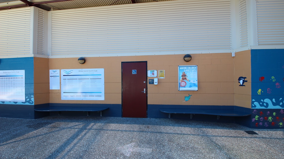 At the entrance, there is a designated area for people with disabilities to enter comfortably. The walls of the building are decorated with various signs and posters that are easy to spot. One specific wooden door has noticeable signage indicating it is for people with disabilities. Additionally, two spacious blue chairs are placed on either side of the main entrance door. At the entrance, there is a designated area for people with disabilities to enter comfortably. The walls of the building are decorated with various signs and posters that are easy to spot. One specific wooden door has noticeable signage indicating it is for people with disabilities. Additionally, two spacious blue chairs are placed on either side of the main entrance door.