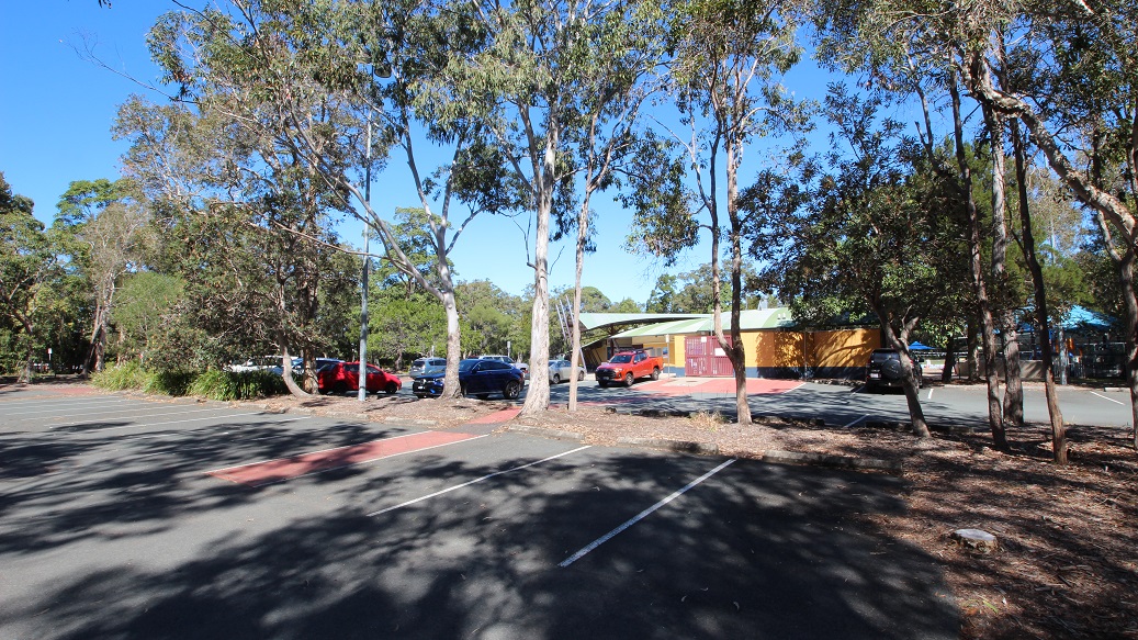 Another angle of the carpark inside the Bribie Island Aquatic and Leisure Centre. The area is filled with tall trees that provide a natural division between the two car spaces. It feels incredibly spacious and well-organized. In the background, you can spot a building painted mostly in yellow, with a striking red front gate. Another angle of the carpark inside the Bribie Island Aquatic and Leisure Centre. The area is filled with tall trees that provide a natural division between the two car spaces. It feels incredibly spacious and well-organized. In the background, you can spot a building painted mostly in yellow, with a striking red front gate.