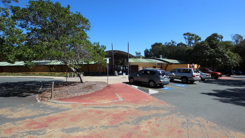 This is the main entrance to the Bribie Island Aquatic and Leisure Centre. In the far right corner, you'll see several parked cars, with two pairs pointing in the same direction. Two poles stand at the very entrance, creating a clear boundary between the outside world and the aquatic and leisure centre beyond. This is the main entrance to the Bribie Island Aquatic and Leisure Centre. In the far right corner, you'll see several parked cars, with two pairs pointing in the same direction. Two poles stand at the very entrance, creating a clear boundary between the outside world and the aquatic and leisure centre beyond.