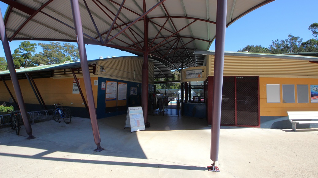A low-set and long building with curved, corrugated iron roof lines can be seen inside the main entrance. On the left side of the entrance, there is signage and bulletin boards, providing useful information to visitors. As you glance to the right, you'll see a small gate with an entry word prominently displayed at its center. In the left corner of the area, two bikes rest leisurely. A low-set and long building with curved, corrugated iron roof lines can be seen inside the main entrance. On the left side of the entrance, there is signage and bulletin boards, providing useful information to visitors. As you glance to the right, you'll see a small gate with an entry word prominently displayed at its center. In the left corner of the area, two bikes rest leisurely.