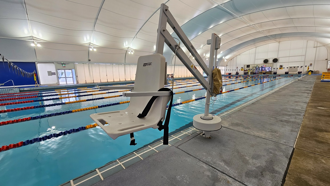In the centre is the 8-lane lap pool, equipped with floating ropes and stairs with railings. A hoist is positioned on the pool deck, along with safety reminder banners on the right. On the far end, a glass door leads to the outdoor pool. The dome-shaped ceiling features floodlights and LED lights. In the centre is the 8-lane lap pool, equipped with floating ropes and stairs with railings. A hoist is positioned on the pool deck, along with safety reminder banners on the right. On the far end, a glass door leads to the outdoor pool. The dome-shaped ceiling features floodlights and LED lights.