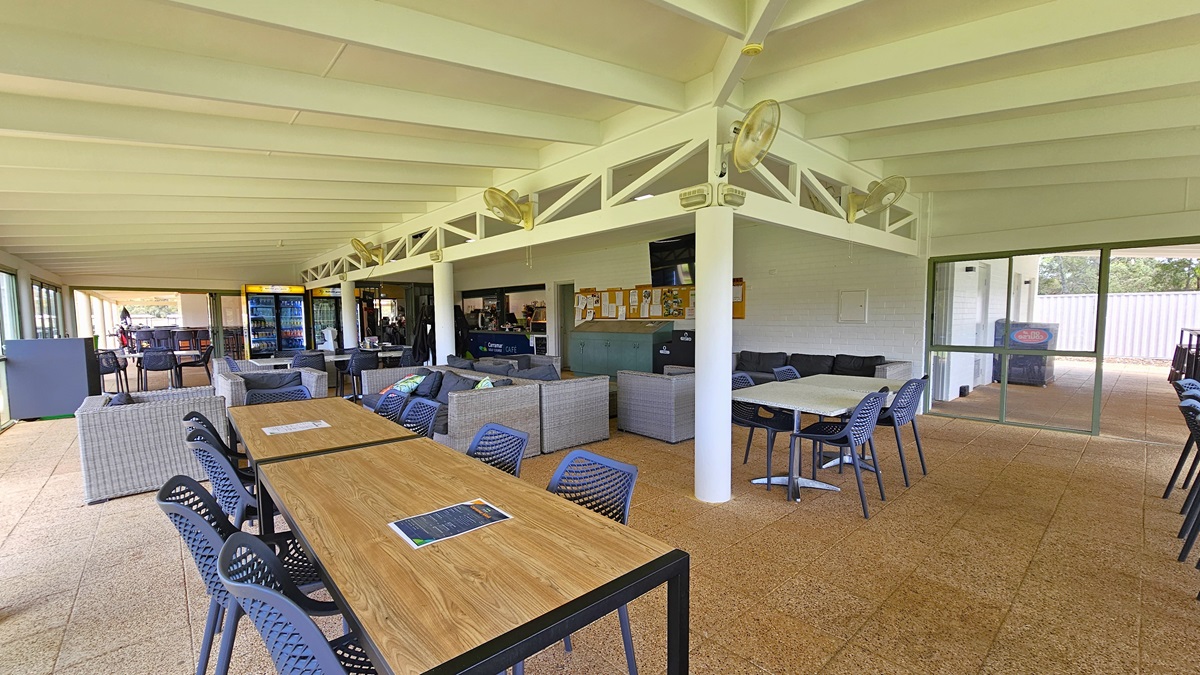 A glass door opens to a wide, spacious green area with manicured grass. Trees and shrubs surround the area, extending through the green. Concrete bricks fill the floor near the cafe. A glass door opens to a wide, spacious green area with manicured grass. Trees and shrubs surround the area, extending through the green. Concrete bricks fill the floor near the cafe.