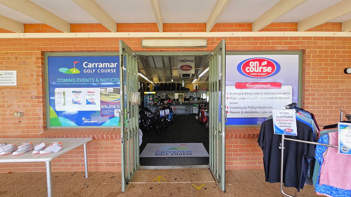 The building's facade is constructed with red bricks, adorned with banners on both sides. On the left, a white table showcases white golf shoes for sale. To the right, men's and ladies' clothing is on display. Inside, the concrete brick exterior transitions to carpeting. A large floor mat with the facility's name is at the doorstep. Retail items are on display inside. The building's facade is constructed with red bricks, adorned with banners on both sides. On the left, a white table showcases white golf shoes for sale. To the right, men's and ladies' clothing is on display. Inside, the concrete brick exterior transitions to carpeting. A large floor mat with the facility's name is at the doorstep. Retail items are on display inside.