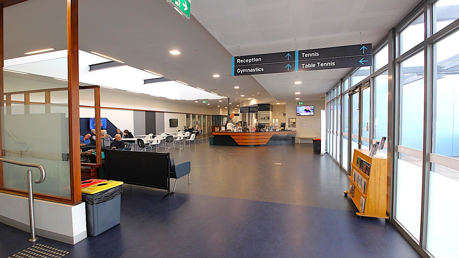 View of the café and seating area from the entrance ramp. The attractive feature of this floor is the skylight above the seating area of the café. The floor is painted in grey and black. The ceiling is white with small, square LED lights. Rubbish bins are placed randomly on this floor for better waste management, and directional signage is large enough to be seen. View of the café and seating area from the entrance ramp. The attractive feature of this floor is the skylight above the seating area of the café. The floor is painted in grey and black. The ceiling is white with small, square LED lights. Rubbish bins are placed randomly on this floor for better waste management, and directional signage is large enough to be seen.