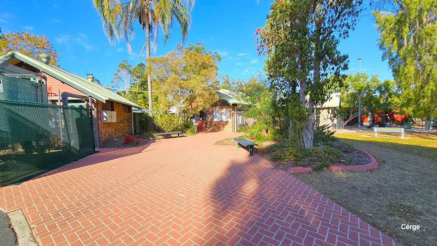 Red brick pathway in Dayboro Pool & Gym. On both edges of the pathway are black benches. The property has low-set buildings with brown tile walls, red wooden front walls, and white roofing structures with round roof vent fans. A green chain link fence encloses the front of the first building with a large grey water tank. Red brick pathway in Dayboro Pool & Gym. On both edges of the pathway are black benches. The property has low-set buildings with brown tile walls, red wooden front walls, and white roofing structures with round roof vent fans. A green chain link fence encloses the front of the first building with a large grey water tank.