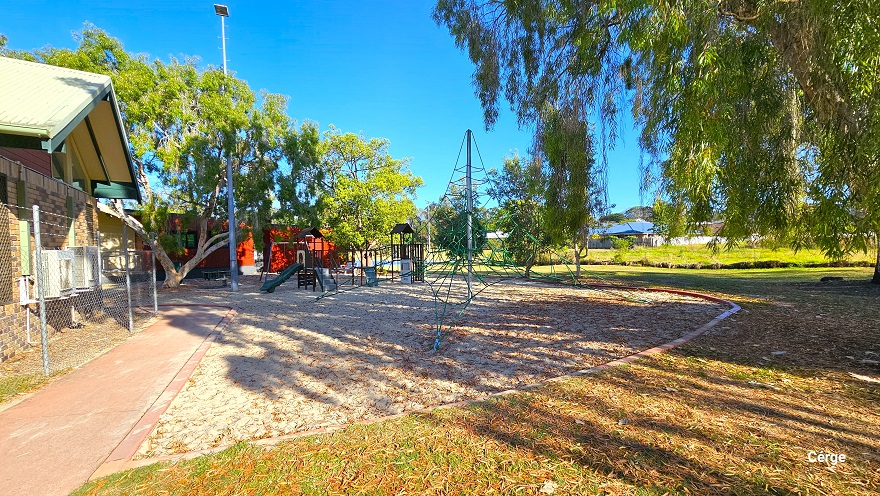 The child’s gym in Dayboro can be distinguished by a circular boundary on its edges and is right outside the chain-linked fence of Dayboro Pool and Gym. A part of the building shows a brown tiled wall. In the middle is an obstacle with green ropes, while to the back are playground climbers and slides. Further beyond is a building with a red wall, and to the right is a large grassland. The child’s gym in Dayboro can be distinguished by a circular boundary on its edges and is right outside the chain-linked fence of Dayboro Pool and Gym. A part of the building shows a brown tiled wall. In the middle is an obstacle with green ropes, while to the back are playground climbers and slides. Further beyond is a building with a red wall, and to the right is a large grassland.