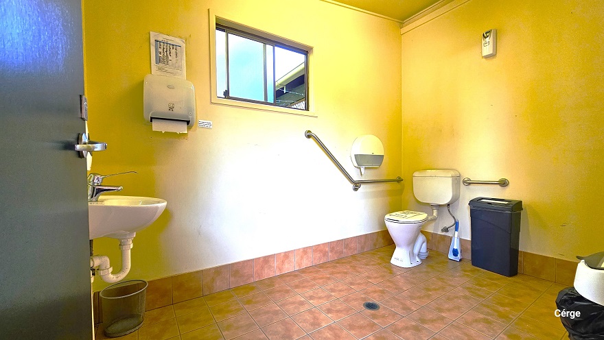 Inside the accessible bathroom in Dayboro Pool and Gym. It has brown floor tile with a faded effect and a white painted wall. The bathroom has a wash basin, two tissue dispensers, grab bars, a toilet brush, and a black garbage bin. On the upper left wall is a glass window for illumination and air circulation. Inside the accessible bathroom in Dayboro Pool and Gym. It has brown floor tile with a faded effect and a white painted wall. The bathroom has a wash basin, two tissue dispensers, grab bars, a toilet brush, and a black garbage bin. On the upper left wall is a glass window for illumination and air circulation.