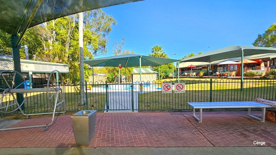 Red brick pathway next to the toddler splash pool enclosed by a green pool fence. Hanging on the green pool fence are the No Running and No Diving white signboards. There is a silver hose reel, a stainless steel wash basin, and a silver metal bench. Further to the left is a long sunshade with an upper side white cover that has several holes as designed. Red brick pathway next to the toddler splash pool enclosed by a green pool fence. Hanging on the green pool fence are the No Running and No Diving white signboards. There is a silver hose reel, a stainless steel wash basin, and a silver metal bench. Further to the left is a long sunshade with an upper side white cover that has several holes as designed.