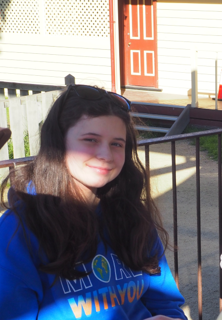 A girl with dark hair sits outdoors, smiling.