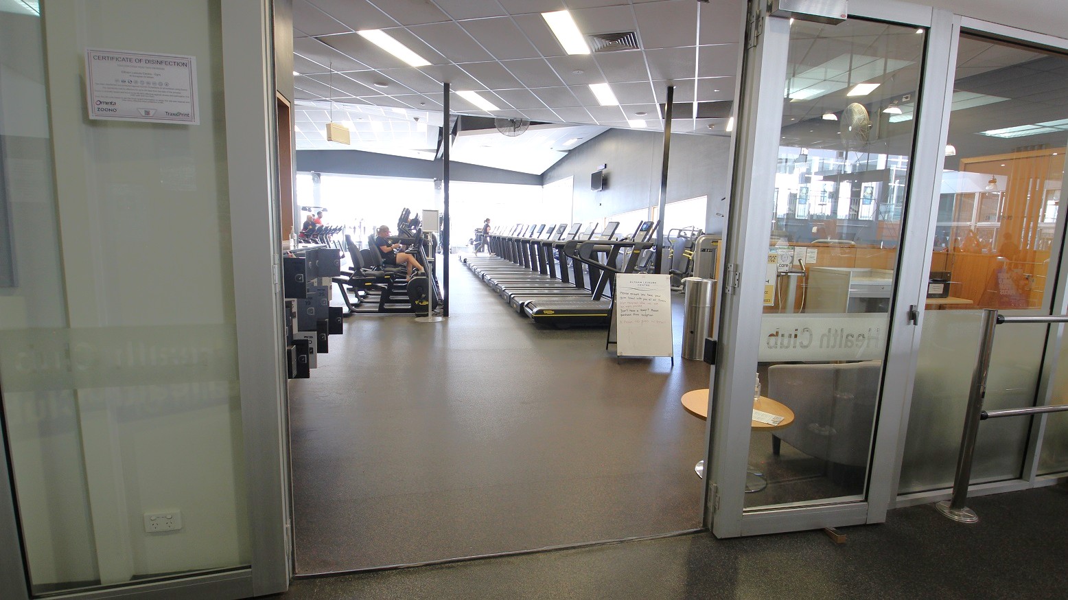 A disinfection certificate is mounted at the left side of the main entrance door of the Gymnasium at Eltham Leisure Centre. Several treadmills are lined directly at the main entrance. A disinfection certificate is mounted at the left side of the main entrance door of the Gymnasium at Eltham Leisure Centre. Several treadmills are lined directly at the main entrance.
