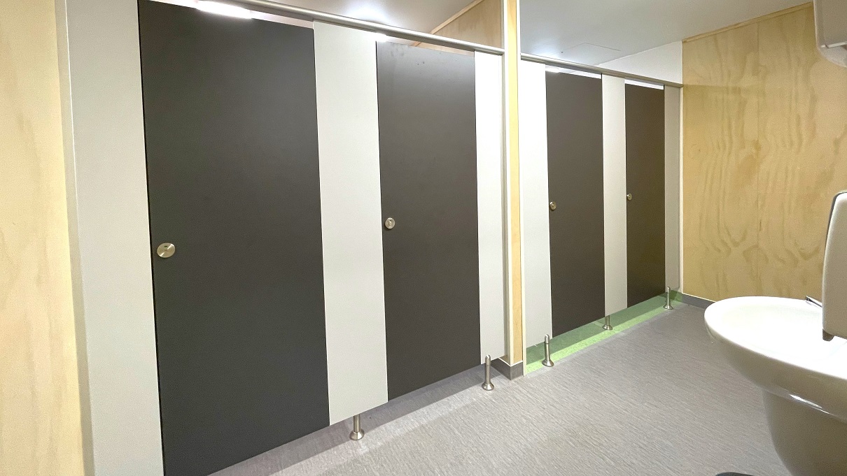 Other bathrooms in Gallagher Recreation Center. The bathroom has smooth, dark brown doors and small circular metal with green and red visual options to notify guests when occupied or not. A wall in the middle separates the bathroom stalls. The bathroom stalls have grey floor tiles, while the other two have light green floor tiles. Outside the bathroom stalls is a low-set hand basin with a liquid hand soap dispenser. Other bathrooms in Gallagher Recreation Center. The bathroom has smooth, dark brown doors and small circular metal with green and red visual options to notify guests when occupied or not. A wall in the middle separates the bathroom stalls. The bathroom stalls have grey floor tiles, while the other two have light green floor tiles. Outside the bathroom stalls is a low-set hand basin with a liquid hand soap dispenser.