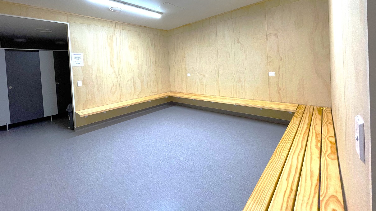 Seating area outside the bathroom stalls in Gallagher Recreation Center. Alongside the walls are four light brown wood planks that serve as seats. Similar to other areas, this has a brown wall and a white ceiling. On the right wall is the light switch. The area is illuminated by a fluorescent light. There is a small, black garbage bin in front of the bathroom stalls. Seating area outside the bathroom stalls in Gallagher Recreation Center. Alongside the walls are four light brown wood planks that serve as seats. Similar to other areas, this has a brown wall and a white ceiling. On the right wall is the light switch. The area is illuminated by a fluorescent light. There is a small, black garbage bin in front of the bathroom stalls.