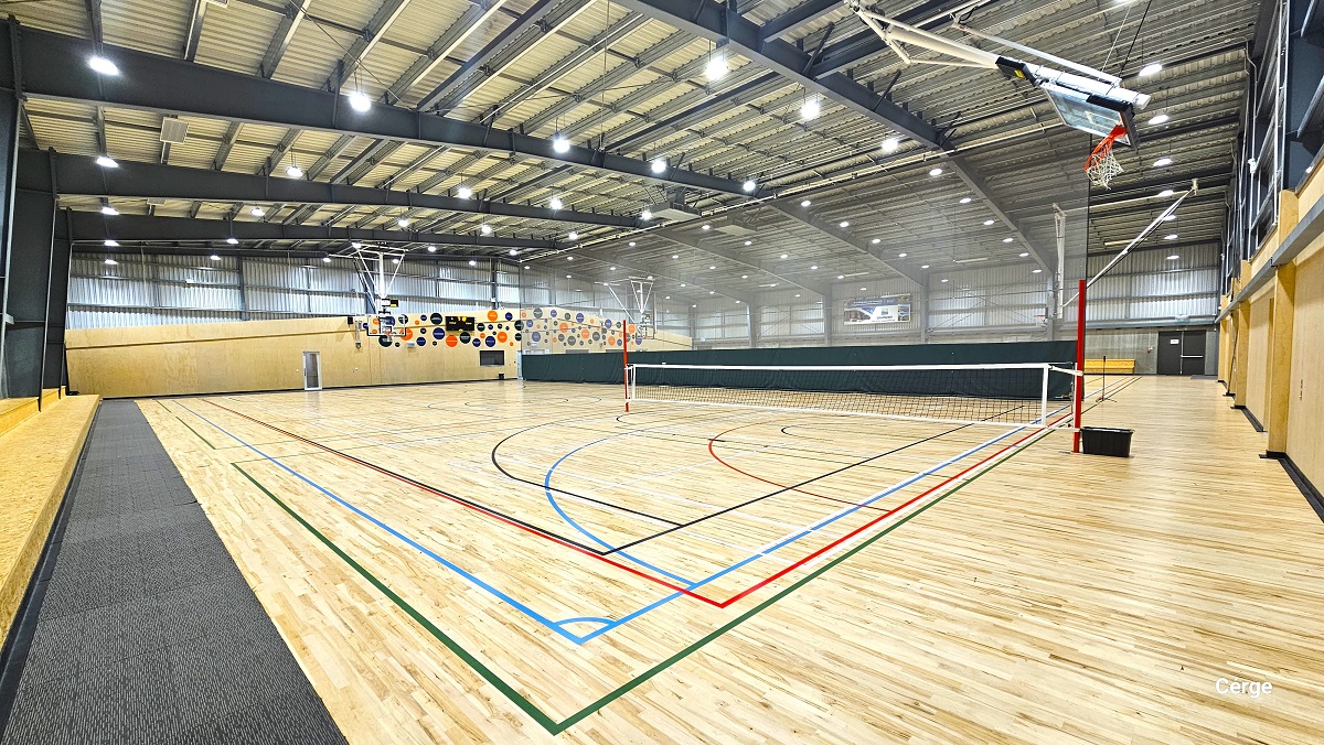 A closer look at the low net wrapped around two red poles placed at opposite ends. The basketball ring is slightly inclined towards the grey corrugated wall. On the left is a two-tiered seating alongside the stadium and grey mats. Also visible from this position are the colorful round designs on the wall above the glass entrance doors. A closer look at the low net wrapped around two red poles placed at opposite ends. The basketball ring is slightly inclined towards the grey corrugated wall. On the left is a two-tiered seating alongside the stadium and grey mats. Also visible from this position are the colorful round designs on the wall above the glass entrance doors.