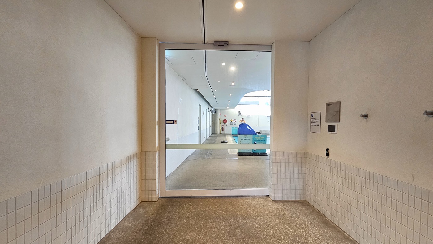 A sliding door provides access to the Hydrotherapy Pool. The walls are entirely white with small tile accents. Signages are present on the right wall. Inside, free standing banners are positioned on the pool deck. The walls and ceiling inside are all white with LED lights.