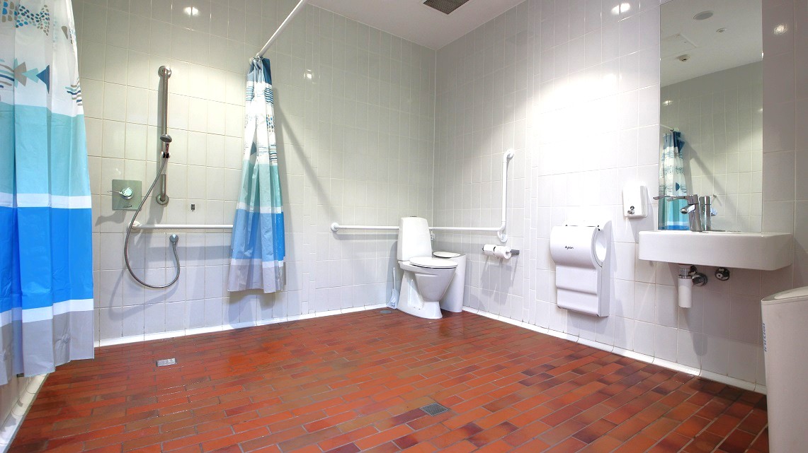 The bathroom is decorated in white and blue, with the patterned curtain hanging around providing privacy.. Simple shades of blue-colored draperies cover the windows in this space. The window coverings soften an area otherwise dominated by smooth, hard surfaces. The toilet, sink, showerhead, toilet paper holder, and towel racks are all visible. The bathroom is decorated in white and blue, with the patterned curtain hanging around providing privacy.. Simple shades of blue-colored draperies cover the windows in this space. The window coverings soften an area otherwise dominated by smooth, hard surfaces. The toilet, sink, showerhead, toilet paper holder, and towel racks are all visible.