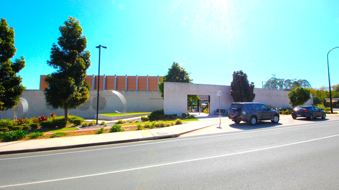 Roadside view of Gympie ARC. The entrance to the Gympie Aquatic Recreation Centre features a distinctive white-brick façade adorned with stainless steel elements. Surrounding gardens and trees further beautify the area, while the color scheme harmoniously blends white, brick, stainless steel, brown, and green elements. Roadside view of Gympie ARC. The entrance to the Gympie Aquatic Recreation Centre features a distinctive white-brick façade adorned with stainless steel elements. Surrounding gardens and trees further beautify the area, while the color scheme harmoniously blends white, brick, stainless steel, brown, and green elements.