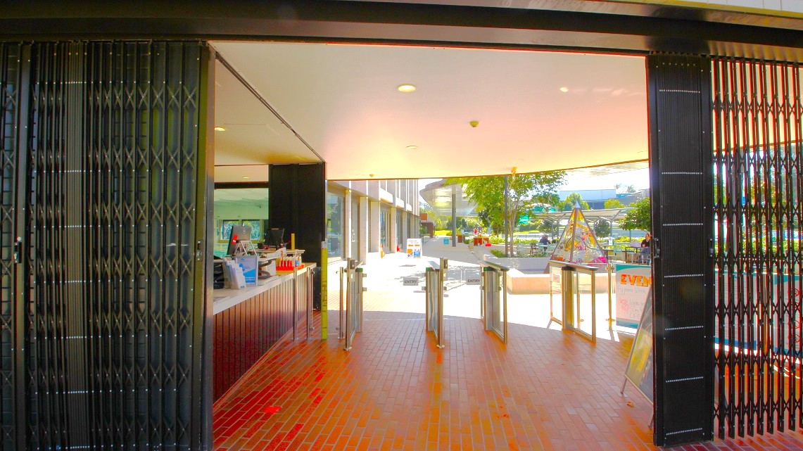 Main entrance of the Gympie ARC. The entrance to the Gympie Aquatic Recreation Centre can be reached through metal grill doors, which are open during the day and securely locked at night. Just to the left of the entrance, you'll find the reception area, a welcoming café, and convenient access to both the indoor pool and the bathrooms. The presence of brick floor tiles adds a touch of durability and aesthetic charm to the space. Main entrance of the Gympie ARC. The entrance to the Gympie Aquatic Recreation Centre can be reached through metal grill doors, which are open during the day and securely locked at night. Just to the left of the entrance, you'll find the reception area, a welcoming café, and convenient access to both the indoor pool and the bathrooms. The presence of brick floor tiles adds a touch of durability and aesthetic charm to the space.
