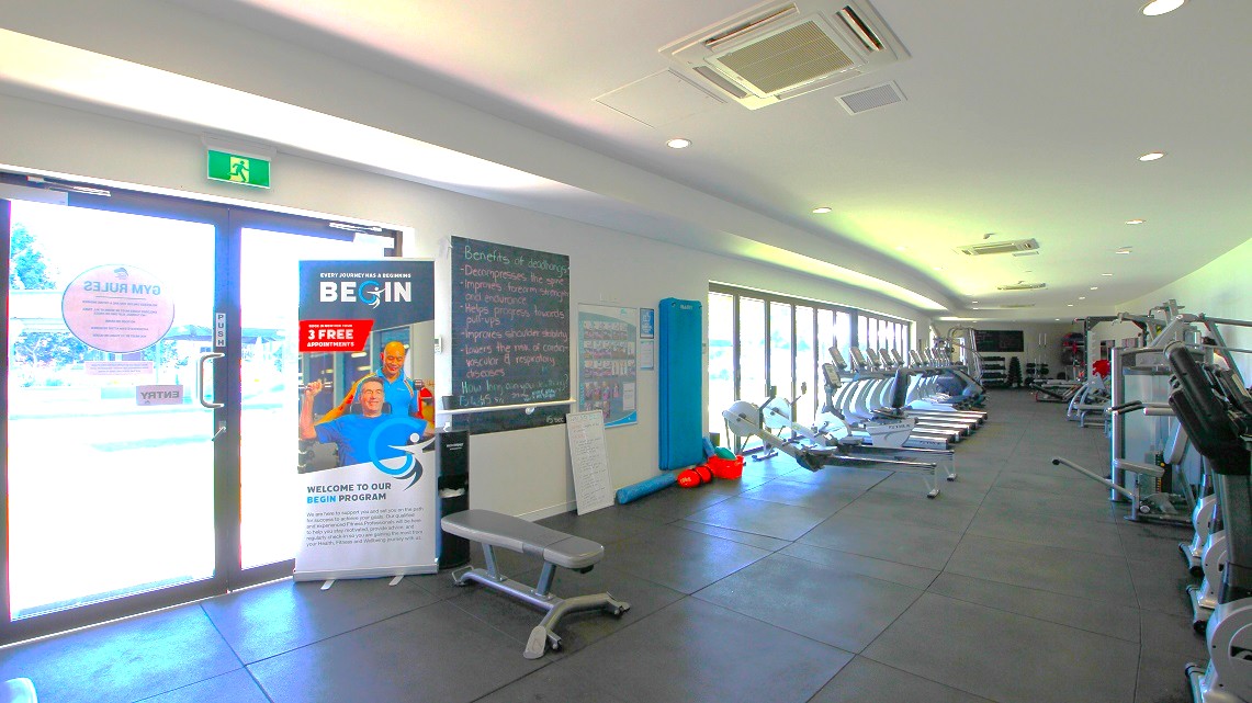 Inside the Gymnasium. The flooring is clad in charcoal-colored rubber matting. Inside the gym, there is a range of fitness equipment, including cardio machines, weight machines, and a dedicated free weight section. The cardio machines are positioned along the left side, running parallel to the windows. On the right side, you'll find additional equipment, like weight machines, arranged in line with the wall's length. Inside the Gymnasium. The flooring is clad in charcoal-colored rubber matting. Inside the gym, there is a range of fitness equipment, including cardio machines, weight machines, and a dedicated free weight section. The cardio machines are positioned along the left side, running parallel to the windows. On the right side, you'll find additional equipment, like weight machines, arranged in line with the wall's length.