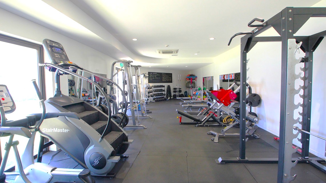 A closer look at the accessible gym equipment. The gym is thoughtfully designed, featuring a well-arranged assortment of cardio machines, weight machines, and a designated space dedicated to free weight exercises. Everything is neatly organized and easily accessible. The walls are painted in a clean and crisp white color, creating a bright and inviting atmosphere. Throughout the entire gym, the illumination is provided by overhead fluorescent lights. A closer look at the accessible gym equipment. The gym is thoughtfully designed, featuring a well-arranged assortment of cardio machines, weight machines, and a designated space dedicated to free weight exercises. Everything is neatly organized and easily accessible. The walls are painted in a clean and crisp white color, creating a bright and inviting atmosphere. Throughout the entire gym, the illumination is provided by overhead fluorescent lights.