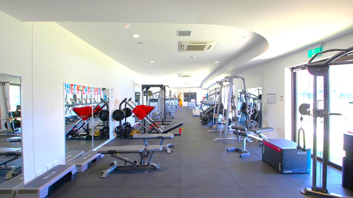 Another angle of the available gym equipment. Various gym equipment, categorized by type, are prominently displayed and neatly organized. Also, the entire floor space is visibly covered by rubber matting. On the lower right side, there's an exit sign positioned above manual glass doors. Another angle of the available gym equipment. Various gym equipment, categorized by type, are prominently displayed and neatly organized. Also, the entire floor space is visibly covered by rubber matting. On the lower right side, there's an exit sign positioned above manual glass doors.