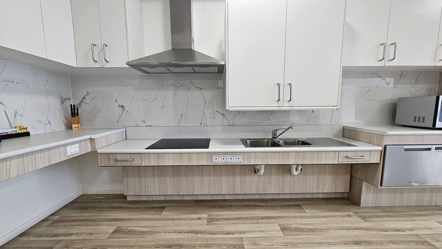 Inside the accommodation, find a kitchen area furnished with wooden cabinets, a kitchen sink, a microwave, and a small fridge, complete with a cooktop and kitchen hood which has been lowered for easier access. Kitchen accessories are neatly placed in the corner. The floor is timber, and the ceiling is white with LED lights. Inside the accommodation, find a kitchen area furnished with wooden cabinets, a kitchen sink, a microwave, and a small fridge, complete with a cooktop and kitchen hood which has been lowered for easier access. Kitchen accessories are neatly placed in the corner. The floor is timber, and the ceiling is white with LED lights.