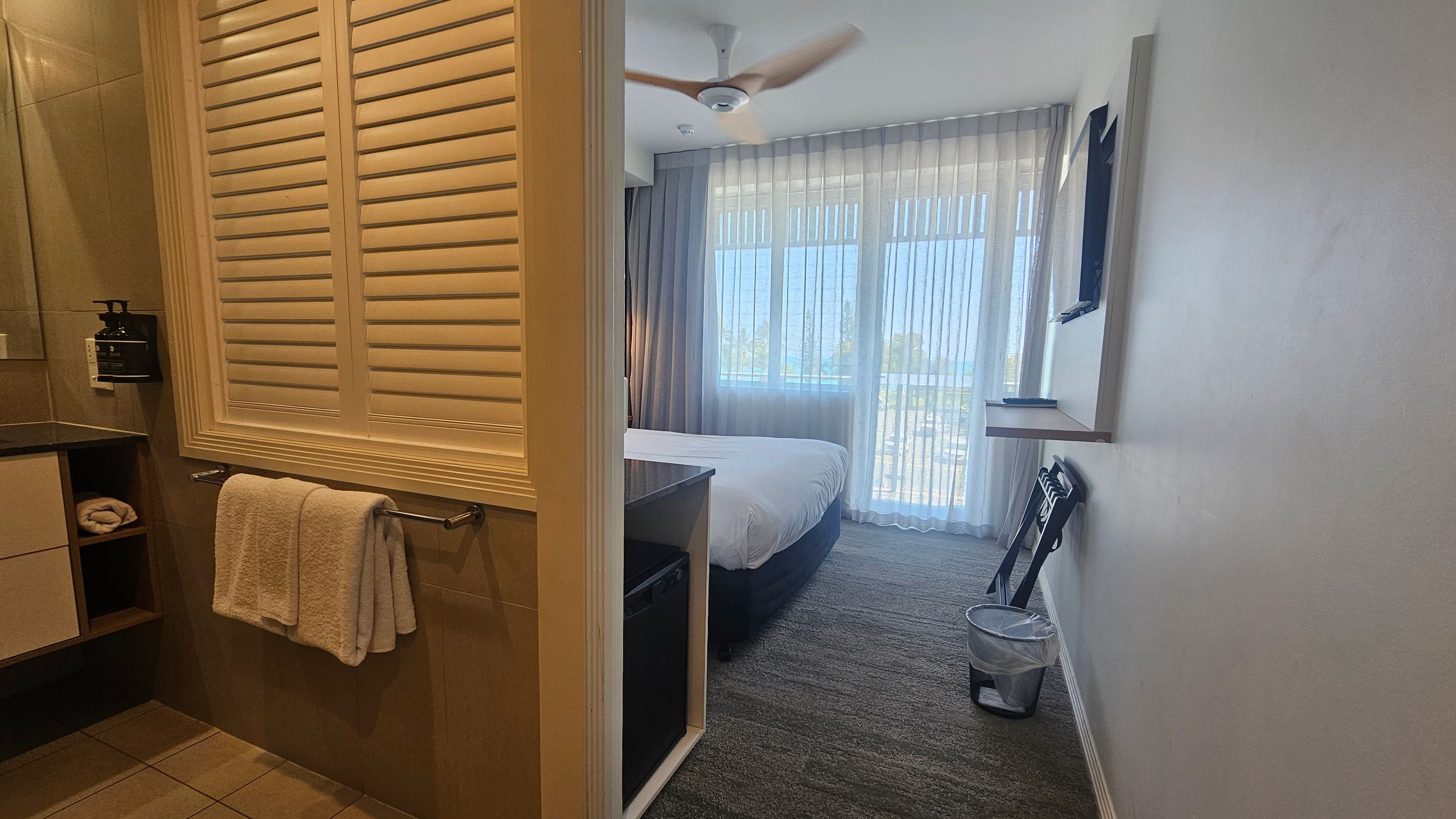 A hallway with two doors, numbered 206 on the left and 207 on the right. The door to room 206 is open, revealing a glimpse of the interior, including a bed, a television mounted on the wall, and a window with sheer curtains. The floor is carpeted in a grey and purple pattern. The ceiling has recessed lighting. Room 207's door is closed and made of wood, with a keycard lock. A hallway with two doors, numbered 206 on the left and 207 on the right. The door to room 206 is open, revealing a glimpse of the interior, including a bed, a television mounted on the wall, and a window with sheer curtains. The floor is carpeted in a grey and purple pattern. The ceiling has recessed lighting. Room 207's door is closed and made of wood, with a keycard lock.