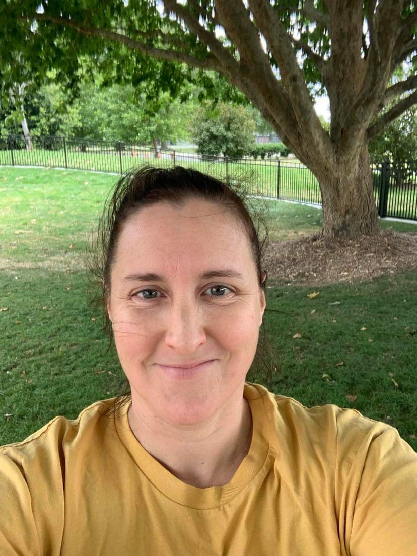 A woman with dark hair wearing a yellow shirt outdoors, smiling. A woman with dark hair wearing a yellow shirt outdoors, smiling.