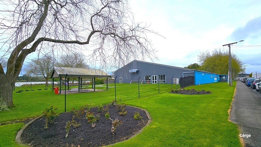 Surrounding the Huntly Aquatic Center is a spacious green field. The property is enclosed in a black, see-through, chain-link fence. Inside the property is a two-seating area with a roof, trees without much foliage, and a lake at the back. Right outside the fence are two circular gardens containing a variety of plants. A cemented pathway separates the parking space in front and the green field of the centre. Surrounding the Huntly Aquatic Center is a spacious green field. The property is enclosed in a black, see-through, chain-link fence. Inside the property is a two-seating area with a roof, trees without much foliage, and a lake at the back. Right outside the fence are two circular gardens containing a variety of plants. A cemented pathway separates the parking space in front and the green field of the centre.