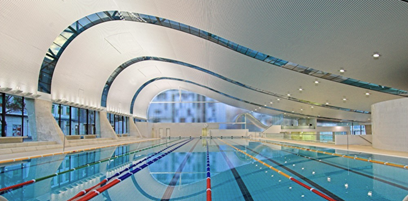 The white ceiling displays a wave-designed porous pattern with glass structures following the ceiling contours and is equipped with LED lights. The glass structures reflect the pool below, adorned with colourful floating ropes. The left side has glass windows providing a view of the outside. The white ceiling displays a wave-designed porous pattern with glass structures following the ceiling contours and is equipped with LED lights. The glass structures reflect the pool below, adorned with colourful floating ropes. The left side has glass windows providing a view of the outside.