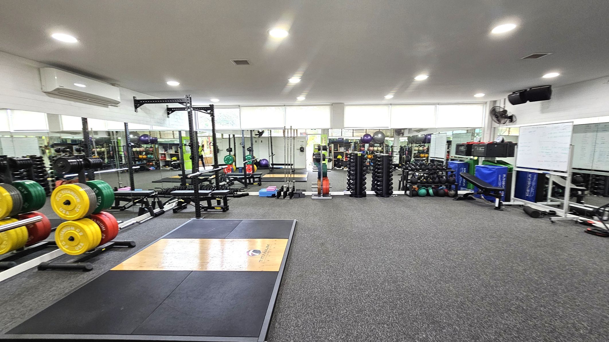 Functional Studio. Functional and Barre Studio. Ivanhoe Aquatic Centre. A spacious gym with a grey carpeted floor and a white ceiling with recessed lighting. On the left, there are weightlifting platforms with colourful weight plates stacked on racks. In the centre, there are various exercise equipment, including benches and dumbbells. The right side features more weights, exercise balls, and a whiteboard. Large mirrors line the walls, reflecting the equipment and adding depth to the space. Functional Studio. Functional and Barre Studio. Ivanhoe Aquatic Centre. A spacious gym with a grey carpeted floor and a white ceiling with recessed lighting. On the left, there are weightlifting platforms with colourful weight plates stacked on racks. In the centre, there are various exercise equipment, including benches and dumbbells. The right side features more weights, exercise balls, and a whiteboard. Large mirrors line the walls, reflecting the equipment and adding depth to the space.