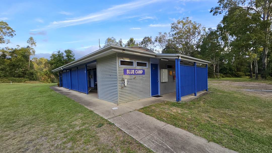 A small, single-storey building with a corrugated metal exterior and a sign reading "Blue Camp" on the front. The structure has blue panels and posts, with a concrete path leading to the entrance. Surrounding the building is a grassy area with trees in the background. The roof is flat, and the building appears to be in a natural, wooded setting. A small, single-storey building with a corrugated metal exterior and a sign reading "Blue Camp" on the front. The structure has blue panels and posts, with a concrete path leading to the entrance. Surrounding the building is a grassy area with trees in the background. The roof is flat, and the building appears to be in a natural, wooded setting.
