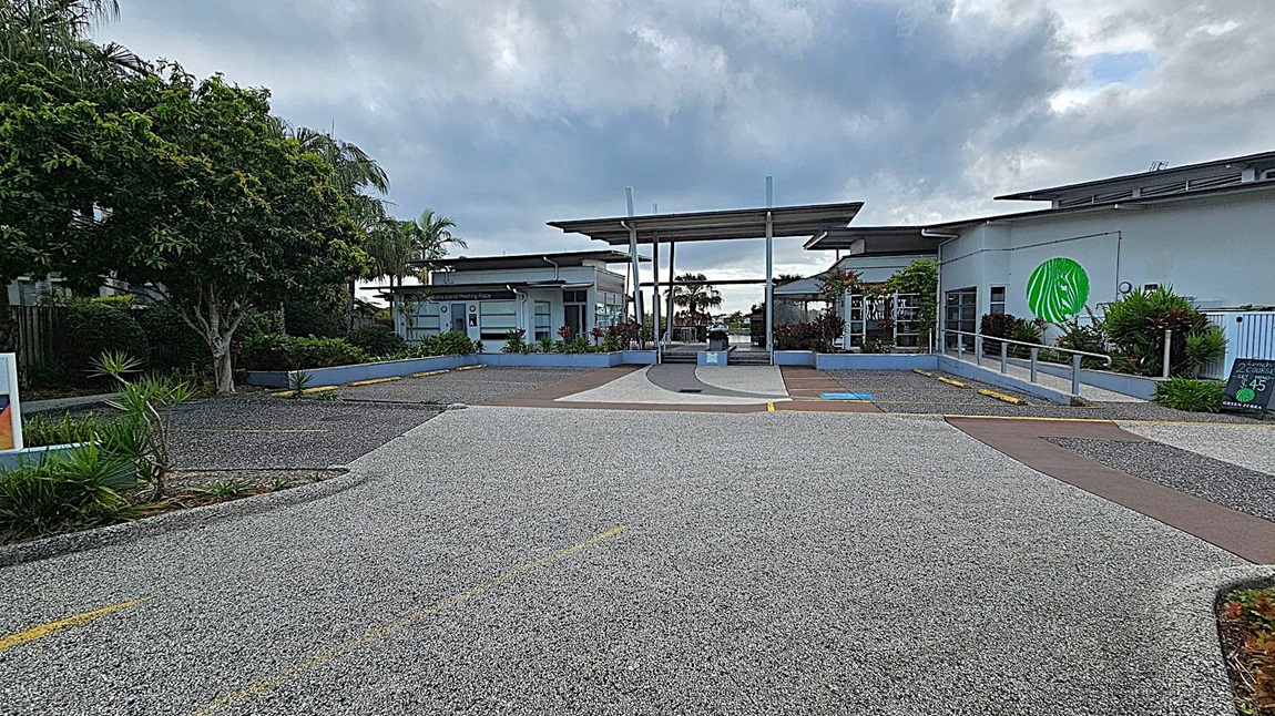 A pathway with yellow directional arrows leads to a modern building with a flat roof. On the left, there are palm trees and a sign with the number 5, indicating "Kawana Island Meeting Place." On the right, a black sign advertises the "Green Zebra Restaurant & Bar" with lunch specials and hours. The area is landscaped with green shrubs and plants. The building features large windows and a logo with a green zebra. A pathway with yellow directional arrows leads to a modern building with a flat roof. On the left, there are palm trees and a sign with the number 5, indicating "Kawana Island Meeting Place." On the right, a black sign advertises the "Green Zebra Restaurant & Bar" with lunch specials and hours. The area is landscaped with green shrubs and plants. The building features large windows and a logo with a green zebra.