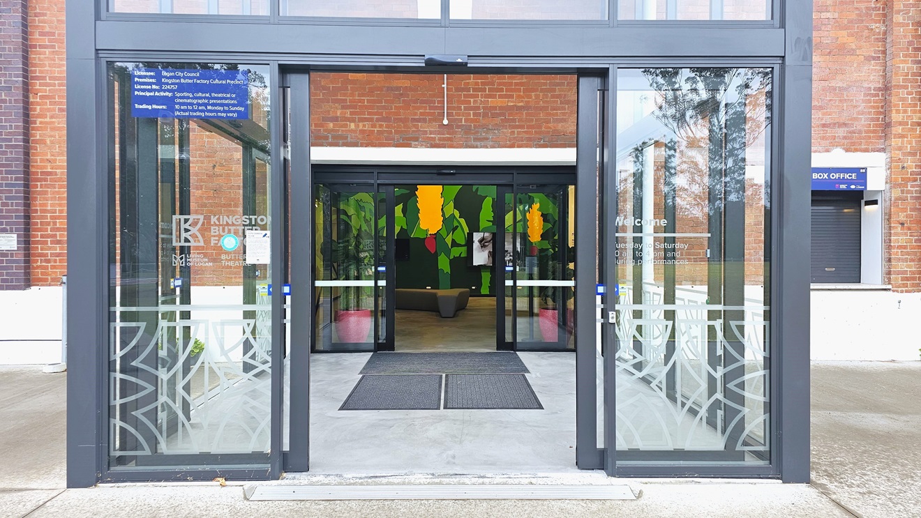 In the middle is a double glass door, furnished with non-slip mats and step free ramp. The front door displays the facility's name and store hours. Inside there is a flat-screen TV mounted on a colorful wall and a seating bench is positioned in the middle. Both sides show the building facade made of red brick walls. A window is visible on the left wall. In the middle is a double glass door, furnished with non-slip mats and step free ramp. The front door displays the facility's name and store hours. Inside there is a flat-screen TV mounted on a colorful wall and a seating bench is positioned in the middle. Both sides show the building facade made of red brick walls. A window is visible on the left wall.