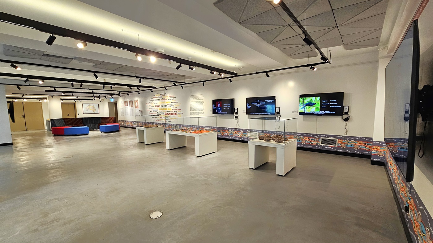 On the right is a spacious area with cushioned seating in the corner. There are three tables with enclosed glass displays. The right wall features meticulously painted wall art. Large flat-screen TVs are mounted on the wall. The ceiling is white with light fixtures and ceiling art decoration. The floor area is made of polished concrete. On the right is a spacious area with cushioned seating in the corner. There are three tables with enclosed glass displays. The right wall features meticulously painted wall art. Large flat-screen TVs are mounted on the wall. The ceiling is white with light fixtures and ceiling art decoration. The floor area is made of polished concrete.