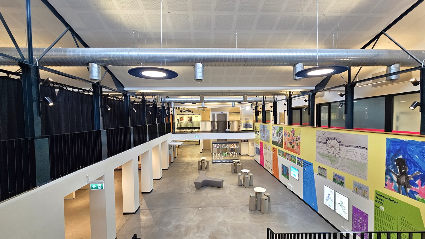 The mezzanine provides a view of the spacious lobby below, featuring a wall adorned with art paintings. Tables and chairs are arranged in the middle, accompanied by a glass display. Navy blue curtains are on the left with low iron railings. To the right, there is another lobby leading to function rooms. The ceiling is white with exposed air-conditioning vents, and stylish circular lights hang from above. The mezzanine provides a view of the spacious lobby below, featuring a wall adorned with art paintings. Tables and chairs are arranged in the middle, accompanied by a glass display. Navy blue curtains are on the left with low iron railings. To the right, there is another lobby leading to function rooms. The ceiling is white with exposed air-conditioning vents, and stylish circular lights hang from above.