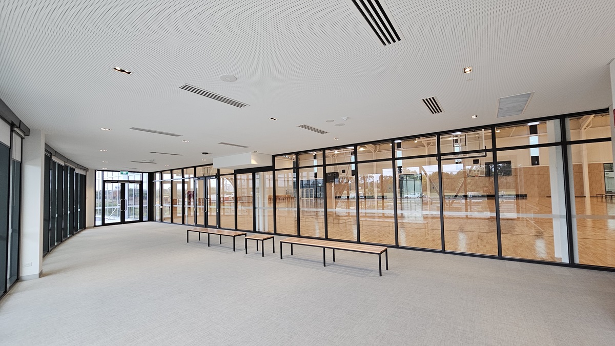 A spacious seating area overlooks the stadium with bench chairs positioned in the middle. To the left, there is a wash area with a small fridge. The wall is made of glass, providing a view of the scenery outside. At the far right is a glass door marked with an "Exit" sign. The floor is firm vinyl, and the ceiling has a white porous design with fluorescent lighting. A spacious seating area overlooks the stadium with bench chairs positioned in the middle. To the left, there is a wash area with a small fridge. The wall is made of glass, providing a view of the scenery outside. At the far right is a glass door marked with an "Exit" sign. The floor is firm vinyl, and the ceiling has a white porous design with fluorescent lighting.