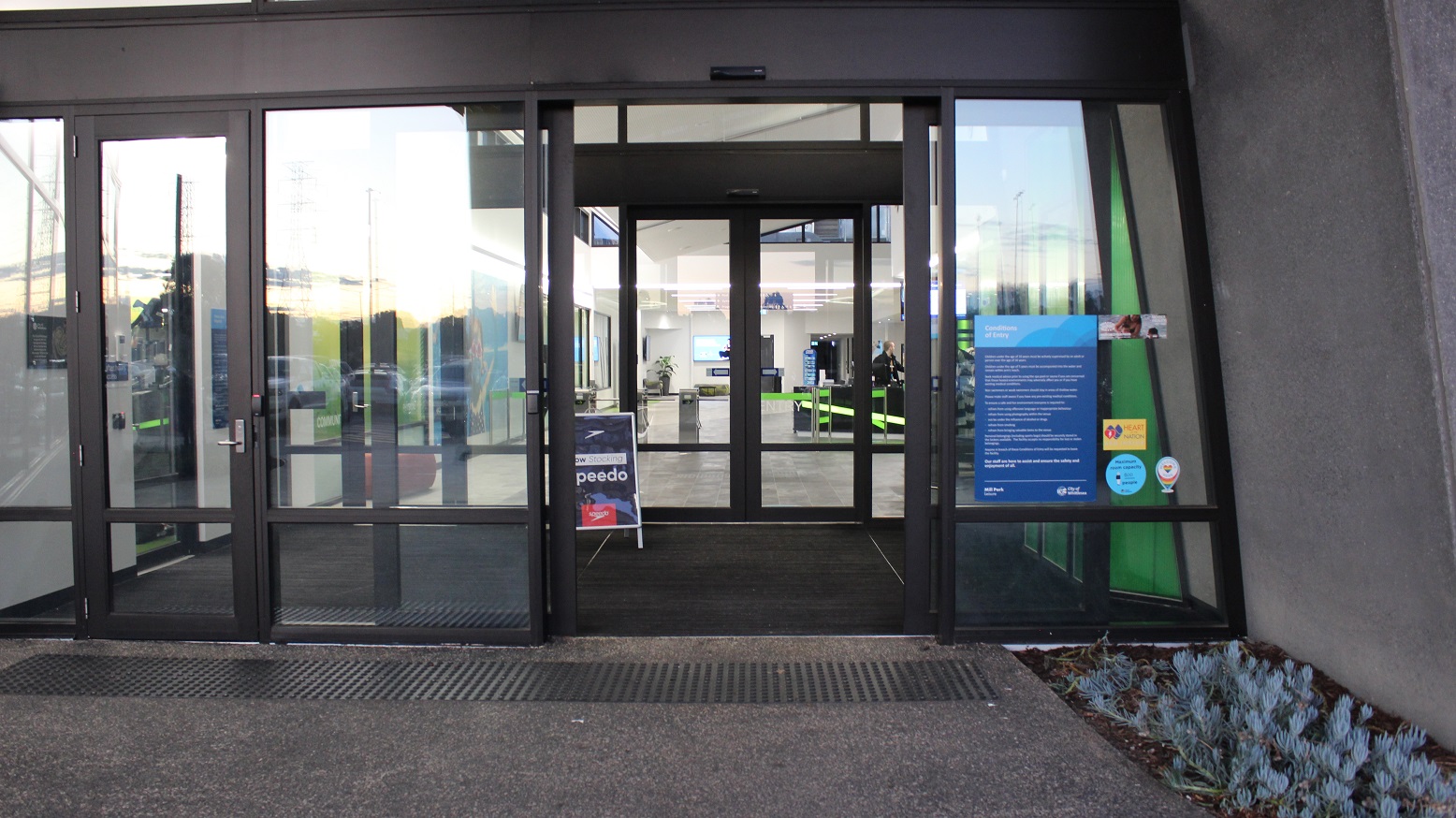 Arrival at Mill Park Leisure, visitors will notice two sets of double doors that are automated for ease of access and a single manual entry door. The doors are made of glass and have black metal edges. On the right side of the manually operating door are the conditions of entry typewritten on blue paper for guests to read and remember while using the venue.