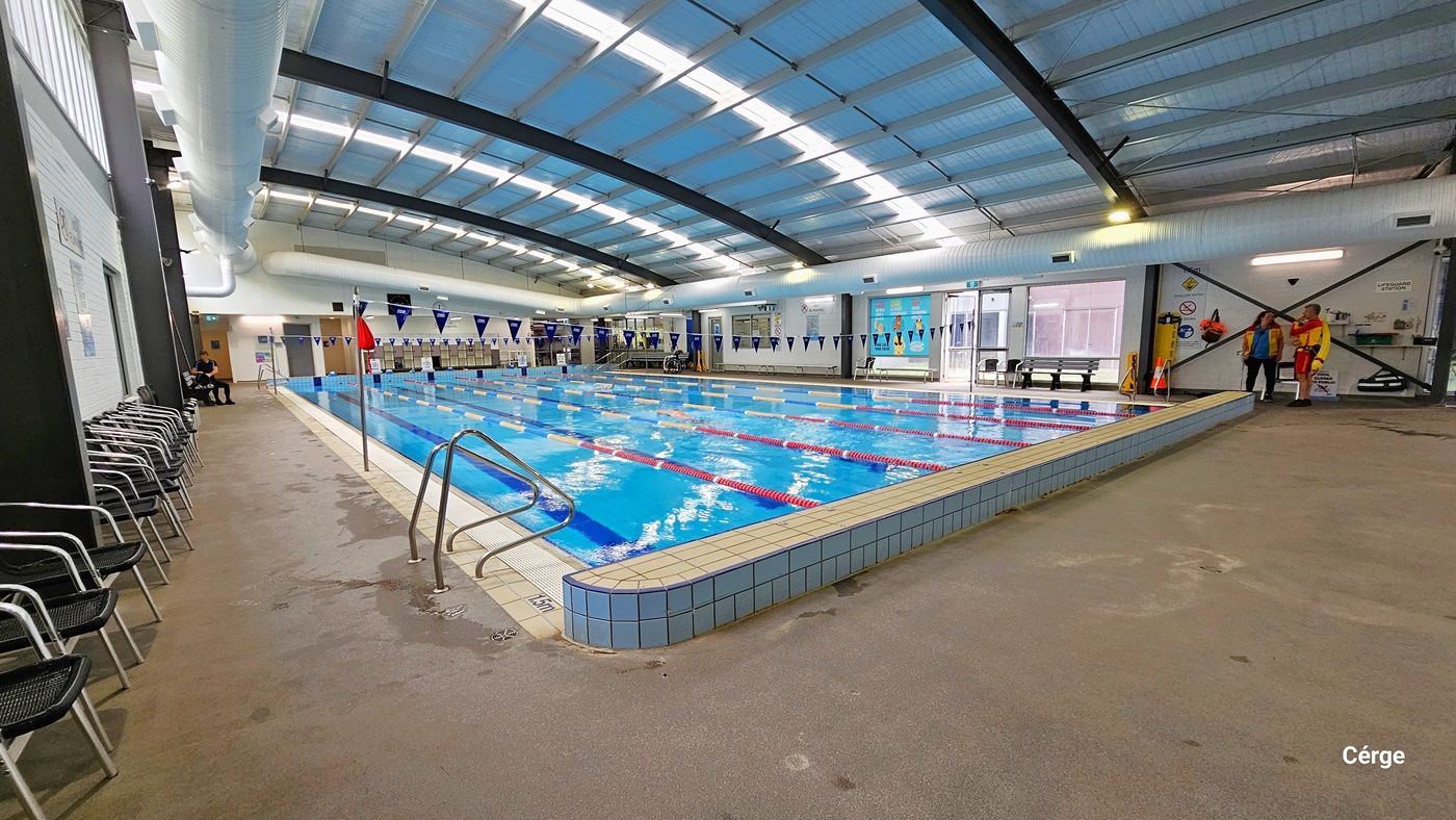 End of the 25m, 6-lane heated indoor pool are two stainless steel grab rails. On the left pool coping is a 1.5m pool depth. On the left pool deck, against the walls, are a line of black plastic chairs with stainless steel handles and legs. On the opposite pool deck are lifeguards wearing yellow and red uniforms, a yellow spine board, an orange cone, and other accessories. End of the 25m, 6-lane heated indoor pool are two stainless steel grab rails. On the left pool coping is a 1.5m pool depth. On the left pool deck, against the walls, are a line of black plastic chairs with stainless steel handles and legs. On the opposite pool deck are lifeguards wearing yellow and red uniforms, a yellow spine board, an orange cone, and other accessories.