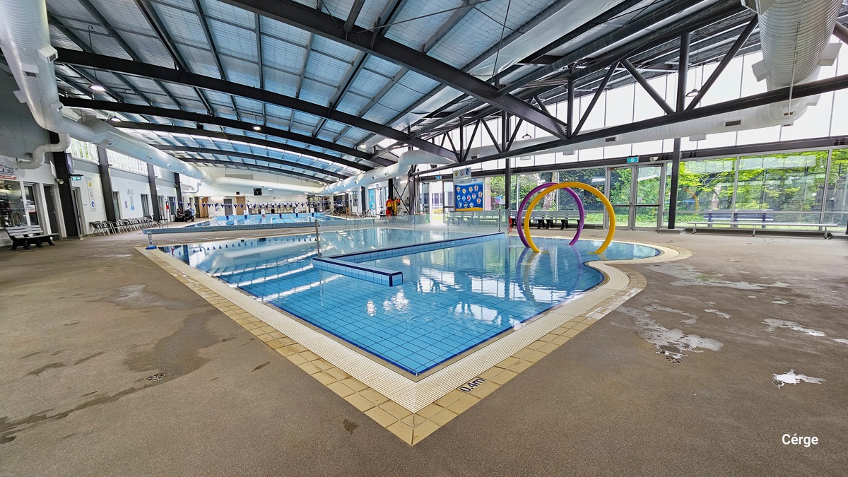Splash water park at Monbulk Aquatic Centre has a concrete floor with rough surface, floor-to-ceiling glass windows that let natural light pass through, a white wall, and a ceiling with black metal beams and large white ventilation ducts. The splash park has a 0.4m depth detailed on the pool coping with white water grating in the middle. An L-shaped tile wall separates the pool, and it encloses the area with large yellow and purple rings. Splash water park at Monbulk Aquatic Centre has a concrete floor with rough surface, floor-to-ceiling glass windows that let natural light pass through, a white wall, and a ceiling with black metal beams and large white ventilation ducts. The splash park has a 0.4m depth detailed on the pool coping with white water grating in the middle. An L-shaped tile wall separates the pool, and it encloses the area with large yellow and purple rings.