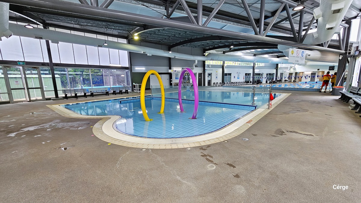 A closer look at the large yellow and purple rings within the Splash water park with 0.4m water depth. Further to the left is another floor-to-ceiling glass window with an exit glass door, which can be identified by the green exit sign. The upper glass wall is made of frosted glass while the lower is transparent. Benches and chairs can be seen all throughout the area. A closer look at the large yellow and purple rings within the Splash water park with 0.4m water depth. Further to the left is another floor-to-ceiling glass window with an exit glass door, which can be identified by the green exit sign. The upper glass wall is made of frosted glass while the lower is transparent. Benches and chairs can be seen all throughout the area.