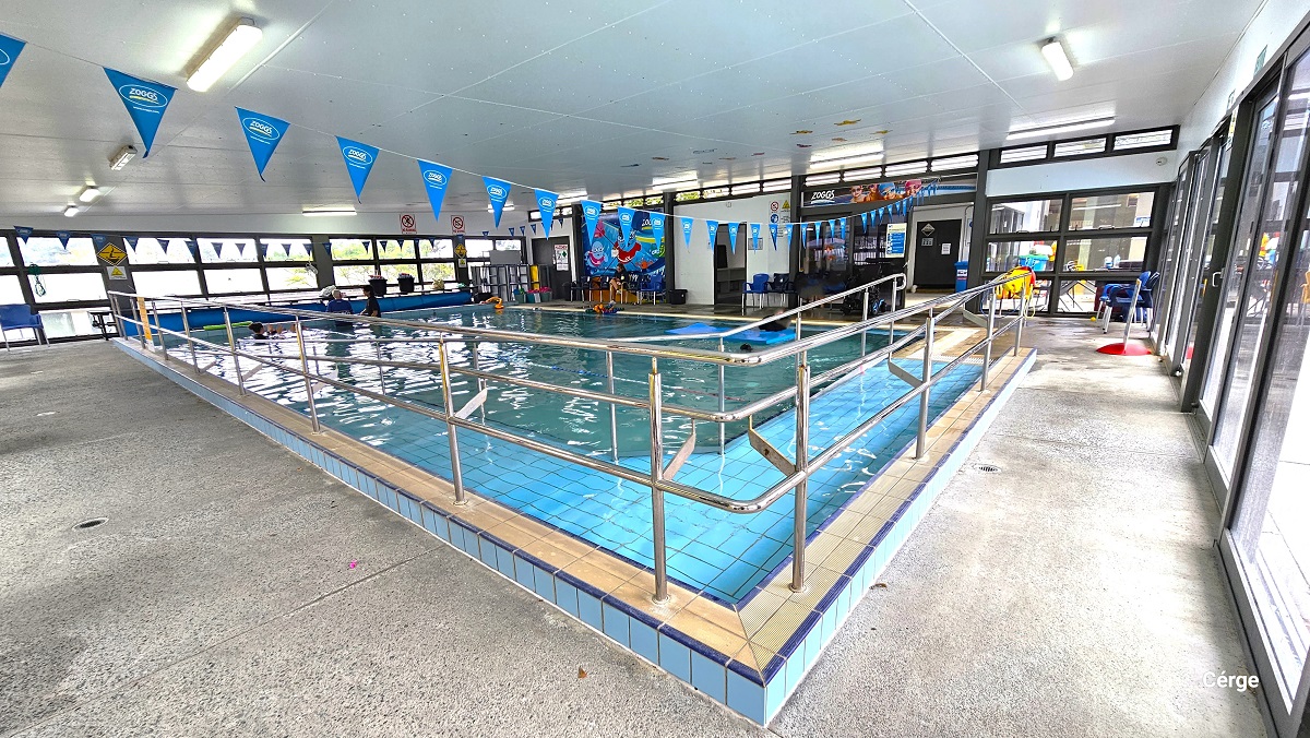 Ramp access with metal handrails in the indoor aquatic pool. Different seating options are accessible throughout the poolside area. From this position, there are two more doors next to the tinted glass sliding doors. On the wall between the two doors is a large poster with cute swimming pool graphics. Ramp access with metal handrails in the indoor aquatic pool. Different seating options are accessible throughout the poolside area. From this position, there are two more doors next to the tinted glass sliding doors. On the wall between the two doors is a large poster with cute swimming pool graphics.