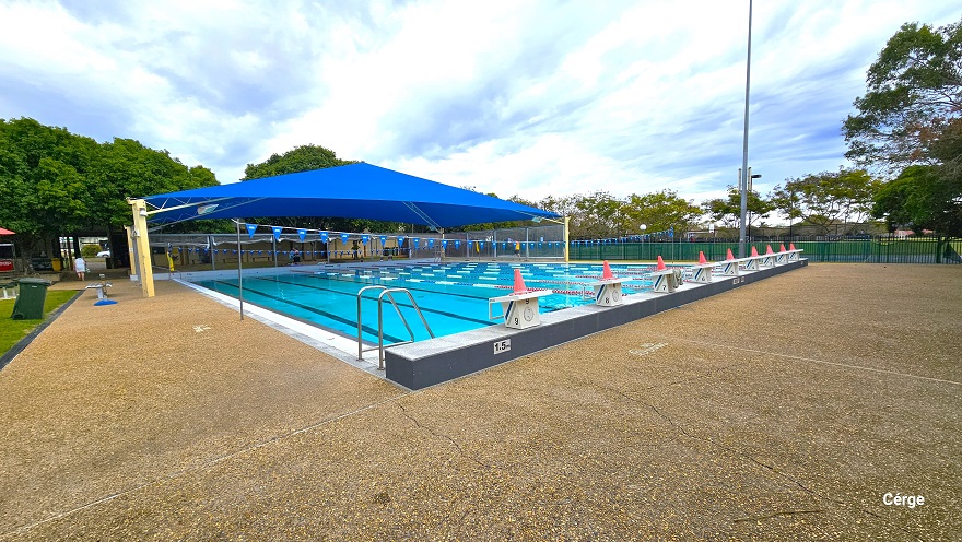 Starting point of the 25m, nine-lap pool at Murrumba Downs Swimming Pool. Each lane has a white diving block that is numbered from 1-9, and on top is an orange cone. Both the starting and end point of the lap pool has an elevated grey floor section. On each side of the pool are pool ladders marked by inverted U stainless steel handles. Strings of triangular blue flags overhang the pool. Starting point of the 25m, nine-lap pool at Murrumba Downs Swimming Pool. Each lane has a white diving block that is numbered from 1-9, and on top is an orange cone. Both the starting and end point of the lap pool has an elevated grey floor section. On each side of the pool are pool ladders marked by inverted U stainless steel handles. Strings of triangular blue flags overhang the pool.