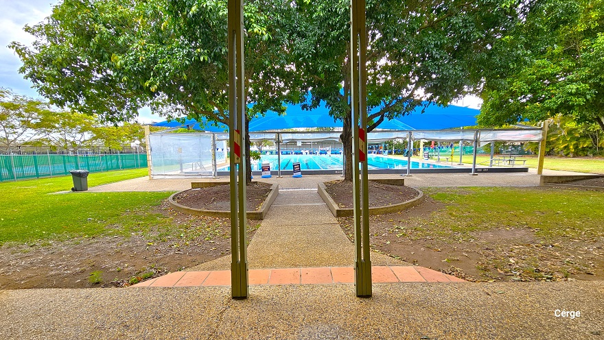 Pool granite pathway with a rough surface that is connected to the ramp access to the bathroom. Before reaching the pool, guests will pass through two semi-circular gardens with trees that have large canopy covers near the pool deck that has a large blue dome structure. There is a grey garbage bin on the left side of the dome covered by a white plastic cover. After the single lane of light brown tile floor are two grey posts with a narrow hole with orange and red stripe markings in the middle. Pool granite pathway with a rough surface that is connected to the ramp access to the bathroom. Before reaching the pool, guests will pass through two semi-circular gardens with trees that have large canopy covers near the pool deck that has a large blue dome structure. There is a grey garbage bin on the left side of the dome covered by a white plastic cover. After the single lane of light brown tile floor are two grey posts with a narrow hole with orange and red stripe markings in the middle.