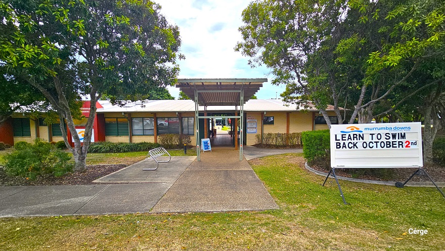 Entry to Murrumba Downs Swimming Pool. On the right side is a white signboard with the name of the facility and the light brown and blue logo. A ‘Learn to Swim Back October 2nd’ can be read on the white sign board. At the left side of the entrance is a stainless steel bike rack. There is a tall entry porch with lime green metal frames and corrugated roofing that connects to the corridor inside the entire facility. Entry to Murrumba Downs Swimming Pool. On the right side is a white signboard with the name of the facility and the light brown and blue logo. A ‘Learn to Swim Back October 2nd’ can be read on the white sign board. At the left side of the entrance is a stainless steel bike rack. There is a tall entry porch with lime green metal frames and corrugated roofing that connects to the corridor inside the entire facility.